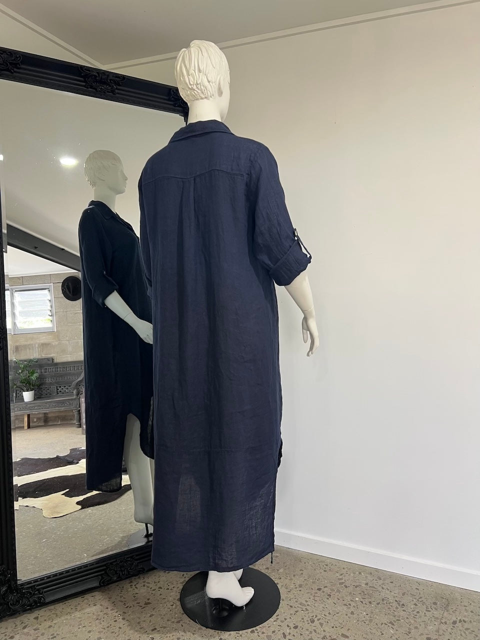 Mannequin wearing a long navy dress in a room with a mirror reflecting another mannequin.