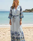 Maxi dress: Miss Goodlife Blue Spirit wrap-neck dress with 3/4 sleeves and tie belt. worn by model in lifestyle shot at the beach LUXAMORE