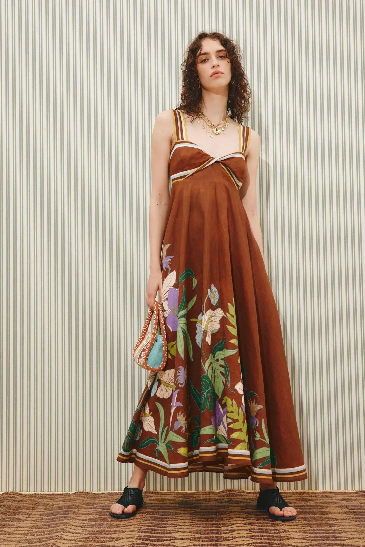 Woman wearing a brown floral dress against a striped wall.